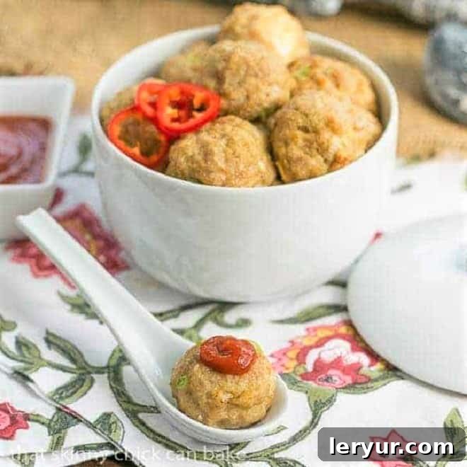 Sesame Ginger Meatballs - Flavorful Asian Chicken Meatballs with Sriracha Dip A serving of golden-brown Sesame Ginger Meatballs in a white ceramic bowl, with one meatball topped with a drizzle of red Sriracha sauce on a small white ceramic spoon, ready to be enjoyed.