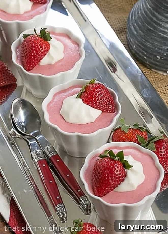 Four servings of Easy Strawberry Mousse in white ramekins, perfectly aligned on a sleek silver tray, ready to be enjoyed with red-handled spoons.