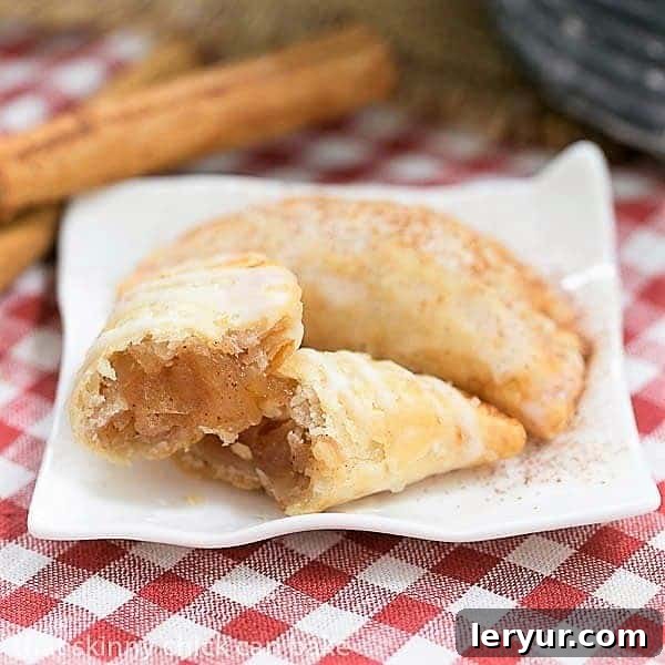 Fried Apple Pies - Easy and delicious hand pies! Two golden brown Fried Apple Pies displayed on a rustic ceramic plate, with one pie carefully broken open to reveal its succulent, cinnamon-spiced apple filling