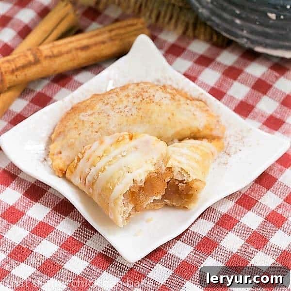 Fried Apple Pies - Easy and delicious hand pies! Two Fried Apple Pies on a white ceramic plate resting on a checkered napkin, with one pie broken open to expose its delightful apple filling