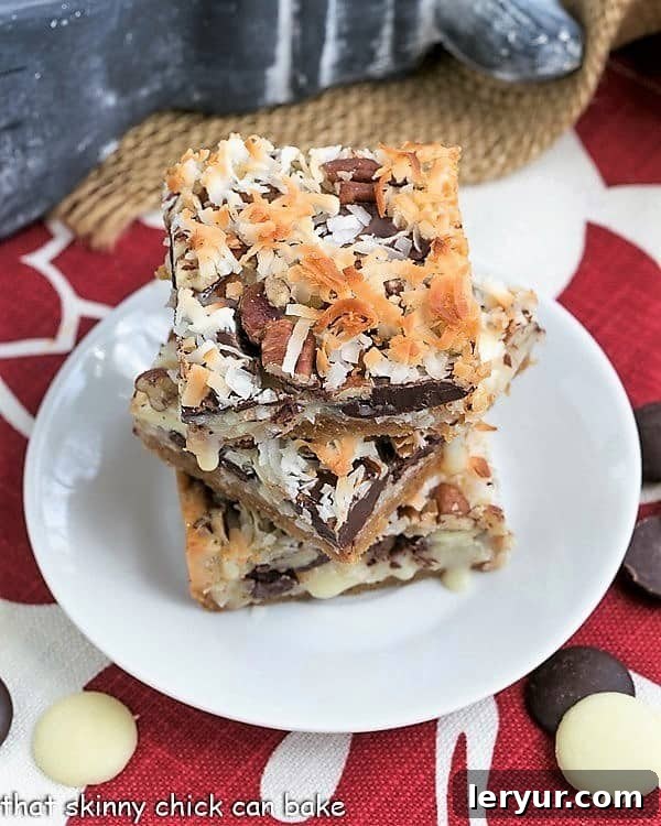 The Best Seven Layer Bars - Graham cracker crust layered with 3 types of chocolate chips, sweetened condensed milk, coconut and pecans! The Best Seven Layer Bars stacked on a round white plate.