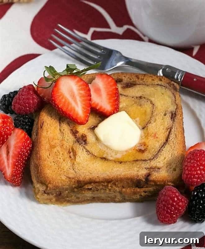Overnight Cinnamon Bread French Toast - a scrumptious, make ahead brunch dish! Overnight Cinnamon Bread French Toast on a white plate with a pat of butter, fresh berries, and a dusting of powdered sugar, ready for enjoyment.