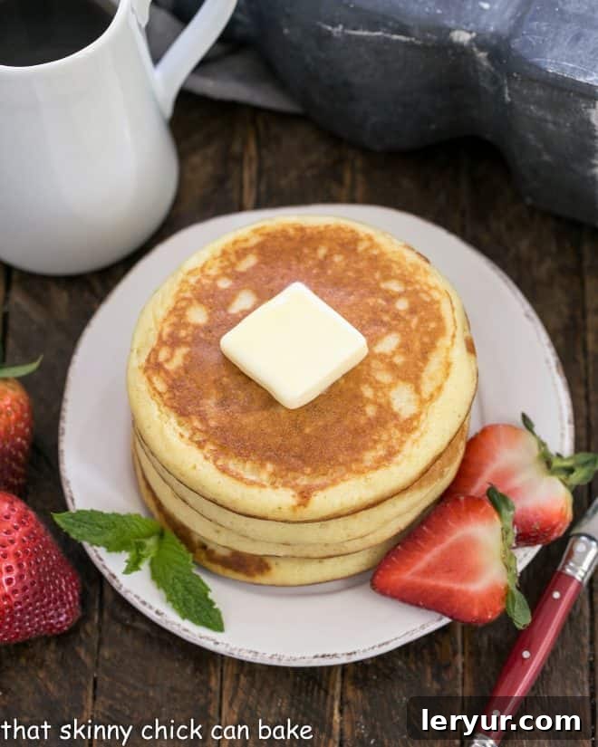Classic Buttermilk Pancakes Recipe - This easy breakfast recipe trumps a box mix every time. A breeze to make with ingredients you'll already find in your kitchen. A stack of golden buttermilk pancakes, lightly browned, topped with a melting pat of butter and garnished with a generous scattering of fresh sliced berries like strawberries and blueberries, ready to be drizzled with syrup.