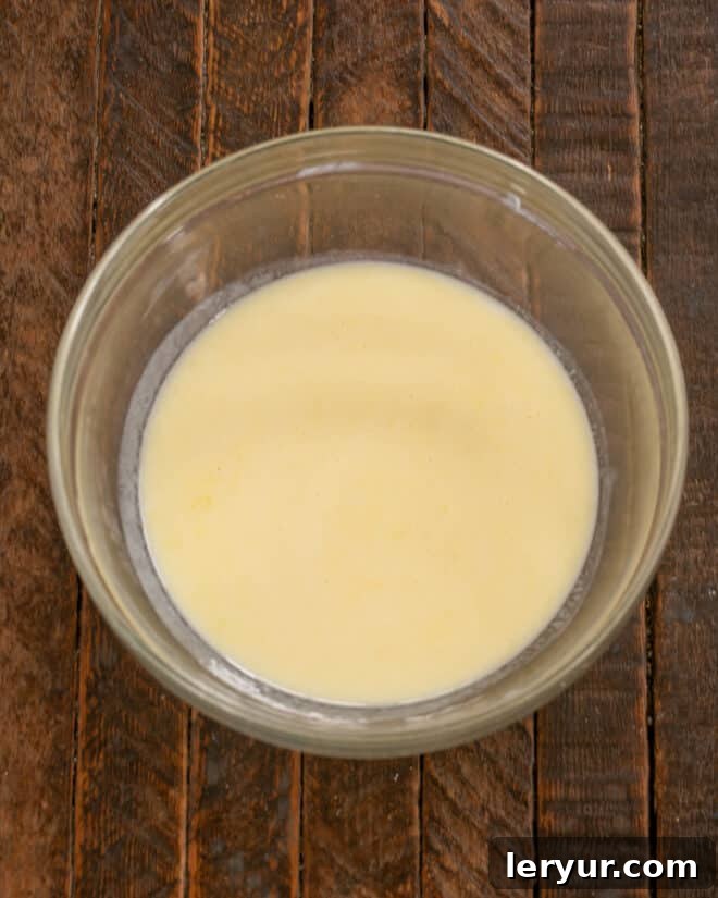 Fluffy Buttermilk Pancakes 4 A close-up of buttermilk being poured into a bowl containing whisked egg, salt, and sugar, illustrating the next step in preparing pancake batter.