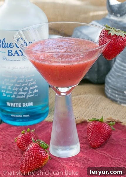 A beautifully presented Hawaiian Sunset Cocktail, garnished with a strawberry, stands in front of a bottle of Blue Chair Bay Rum, ready to be enjoyed.