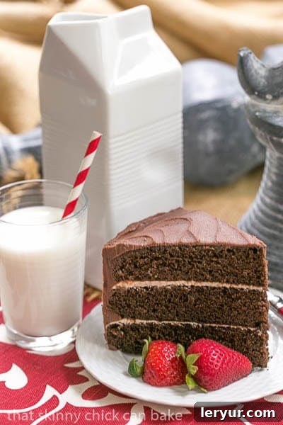 A delightful slice of Triple Layer Chocolate Cake with rich Vanilla Buttercream, served on a crisp white plate, perfectly complemented by a refreshing glass of cold milk. This inviting image captures the essence of a perfect dessert moment.
