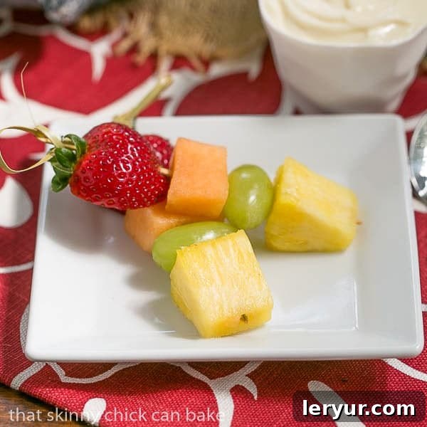 Fruit Skewers with White Chocolate Mascarpone Dip - A dreamy dip to accompany vibrant fresh fruit kebabs Two perfectly assembled fruit kebabs rest next to a ramekin of white chocolate mascarpone dip on a square white plate, ready to be enjoyed.