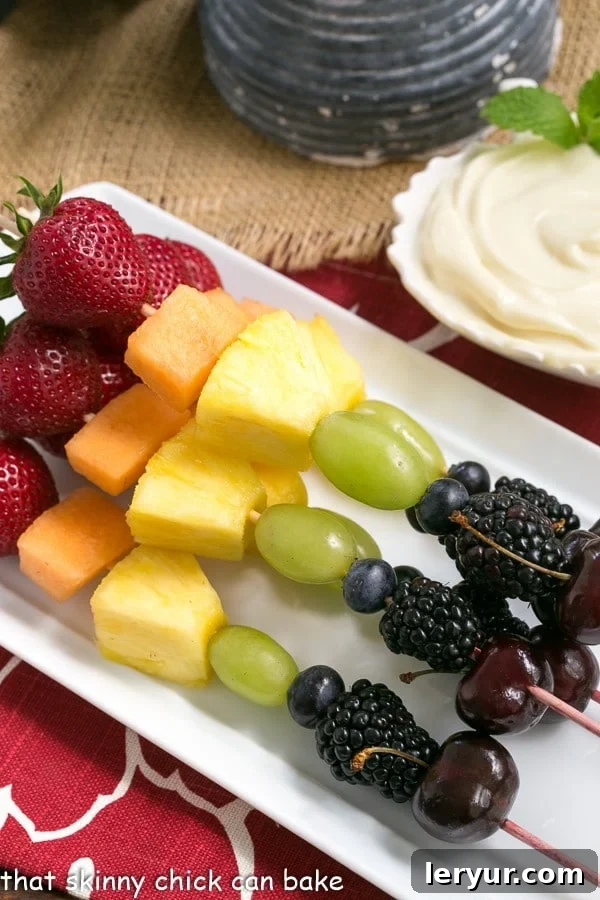 Rainbow Fruit Kabobs with White Chocolate Mascarpone Dip - A dreamy dip to accompany vibrant fresh fruit kebabs A vibrant platter of rainbow fruit kebabs served with a creamy white chocolate mascarpone dip on a rectangular white ceramic tray.