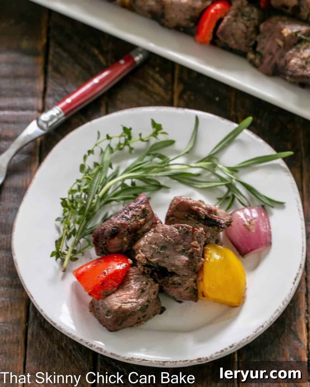 Overhead view of lamb off the skewers on a round white plate with herbs.