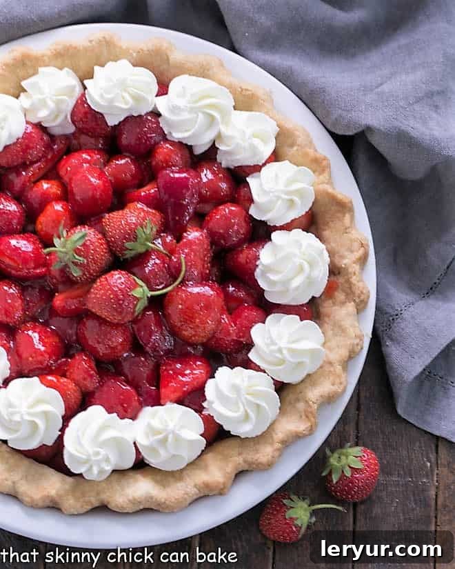 Fresh Strawberry Pie - Luscious ripe strawberries, a fresh berry glaze and a buttery pastry crust form this delicious fresh strawberry pie! Partial overhead view of a strawberry pie adorned with elegant dollops of whipped cream, ready to be served