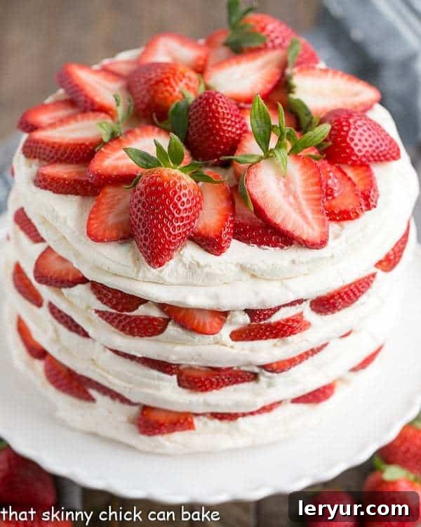 Fresh Strawberry Meringue Cake - A luscious dessert with layers of baked meringue, fresh strawberries and mascarpone whipped cream! Stunning Fresh Strawberry Meringue Cake on a white cake plate, generously garnished with a pile of vibrant sliced fresh strawberries on top.
