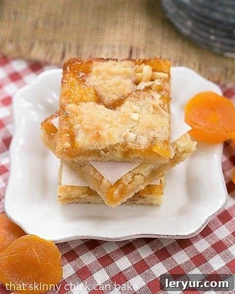 Coconut Apricot Bars - Scrumptious layered jam bars with coconut, almonds and apricot preserves Coconut Apricot Bars garnished with dried apricots on a small square plate.