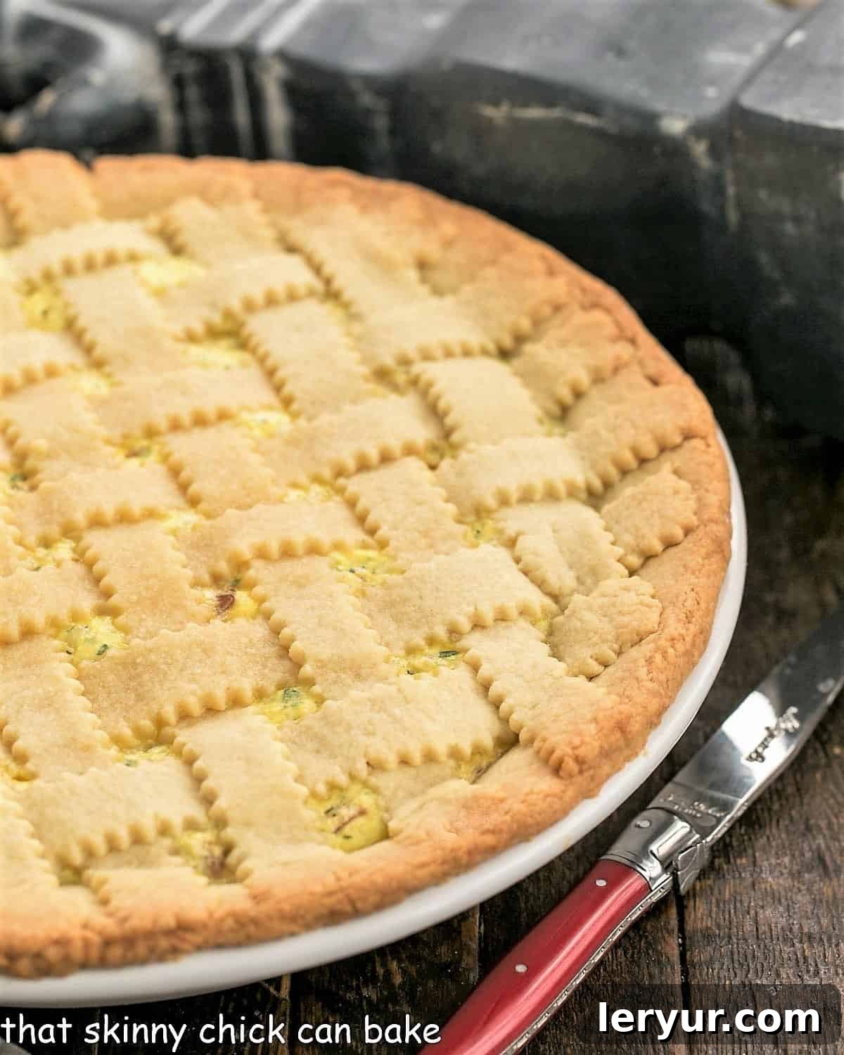 Close view of uncut pizza rustica in a white ceramic pie plate with a red handle knife.