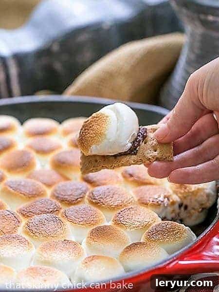 Skillet S'mores Dip with a spoonful scooped up on a graham cracker, showing the gooey marshmallow and melted chocolate.