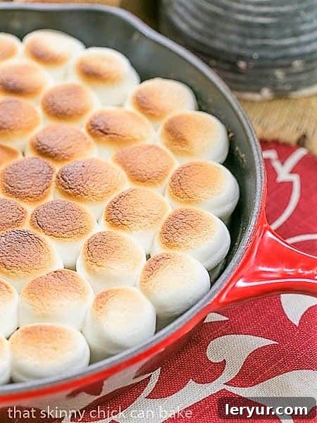 Close view of Skillet S'mores Dip in a red pan, showing the beautifully golden-brown, bubbly marshmallow topping.