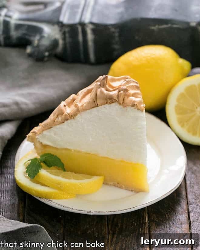 Mile High Lemon Meringue Pie - Luscious lemon filled pastry crust topped with a pillow of fluffy meringue Slice of Mile High Lemon Meringue Pie on a white dessert plate garnished with lemon slices and mint sprigs