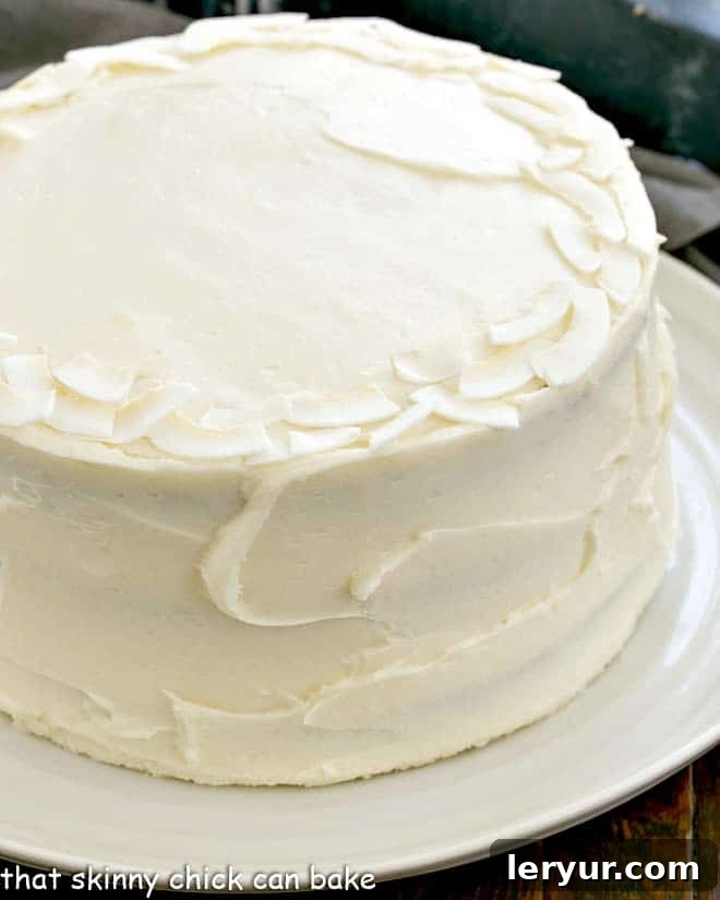 Decadent Italian Cream Cake 3 A beautiful side profile view of an Italian Cream Cake, showcasing the distinct layers of moist coconut cake and thick cream cheese frosting, elegantly placed on a white serving platter.