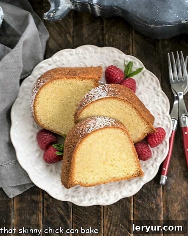 Overhead view of a beautifully baked Sour Cream Pound Cake presented on a white serving plate, garnished with fresh raspberries and a sprig of mint for a vibrant touch.