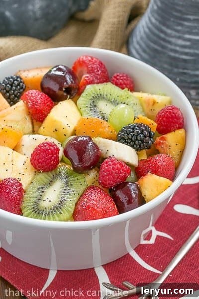 Zesty Honey-Lime Fruit Medley 7 A beautifully arranged white bowl filled with colorful fresh fruit and a glistening poppy seed dressing, resting on a rustic red and white patterned napkin.