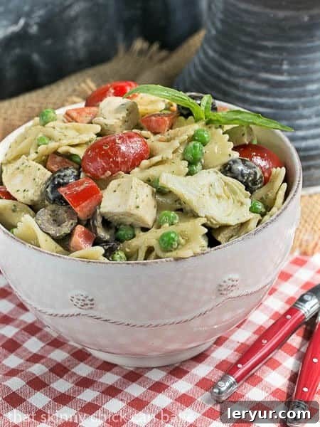 Close-up of a generous portion of Pesto Pasta Salad nestled in a pristine white bowl, accompanied by two red-handled forks, inviting you to dig in.
