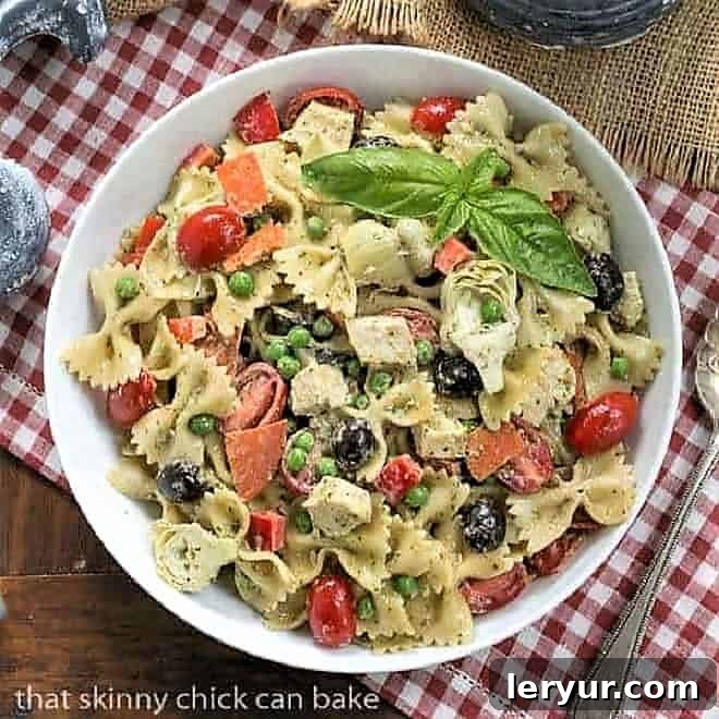 Overhead view of a beautifully presented Pesto Pasta Salad in a white serving bowl, resting on a classic red and white checked napkin.