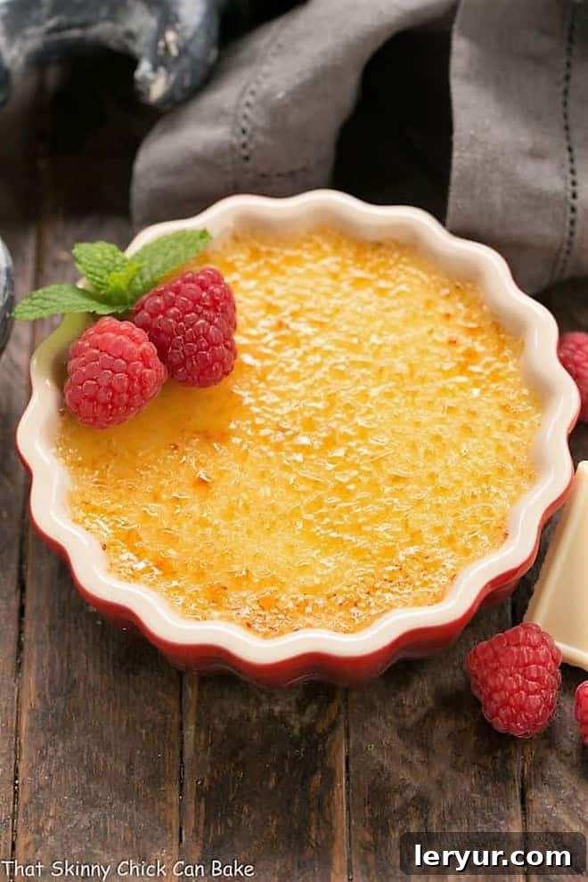 White Chocolate Crème Brûlée in a red ramekin. A perfect, golden-brown caramelized sugar topping sits atop a creamy white custard, garnished with fresh berries.