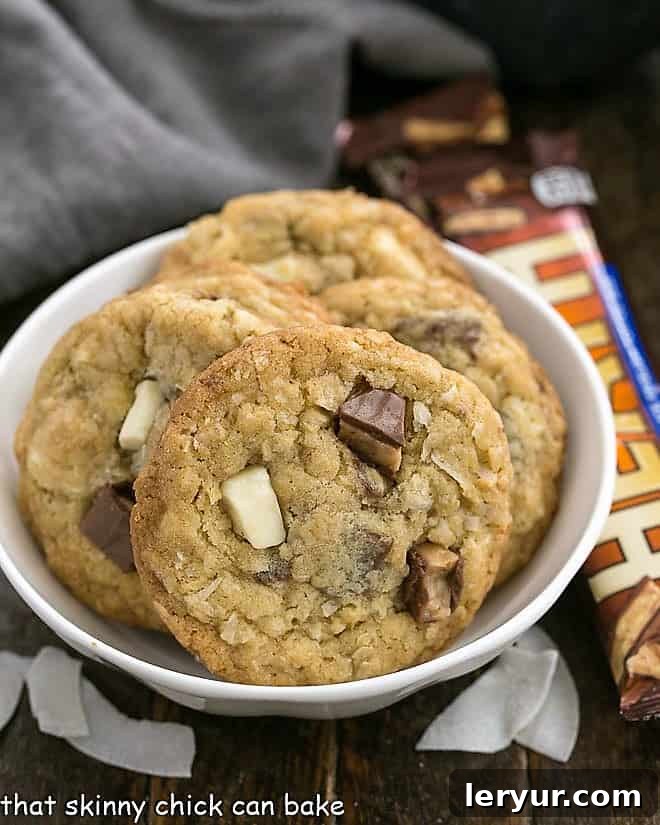 Chewy Oatmeal Toffee Cookies with a coconut bonus - fabulous flavors and textures in every bite make for truly irresistible cookies! A crisp white bowl overflowing with freshly baked Chewy Oatmeal Toffee Cookies, highlighting their golden edges and the enticing blend of white chocolate and toffee within each cookie.