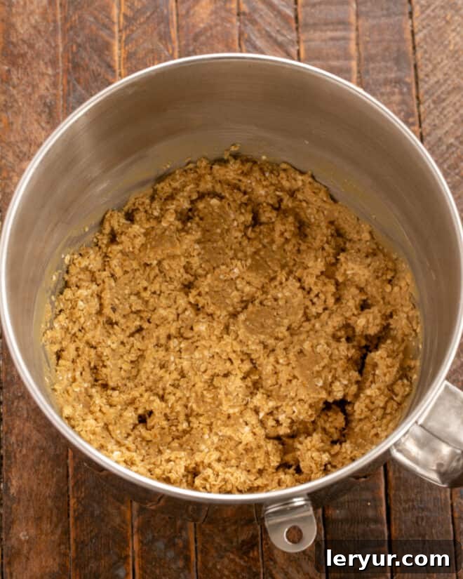 Chewy Oatmeal Caramel Delights 4 Overhead process shot showing the next step in cookie preparation: gradually mixing in the dry ingredients (flour, baking soda, and salt) into the wet mixture, followed by the quick oats until just incorporated.