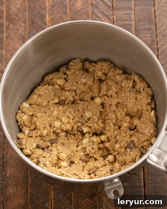 Chewy Oatmeal Caramel Delights 6 Overhead process shot depicting the last steps: mixing the fully loaded cookie dough, then scooping uniform balls onto a parchment-lined baking sheet, ready to be baked to golden perfection and enjoyed.