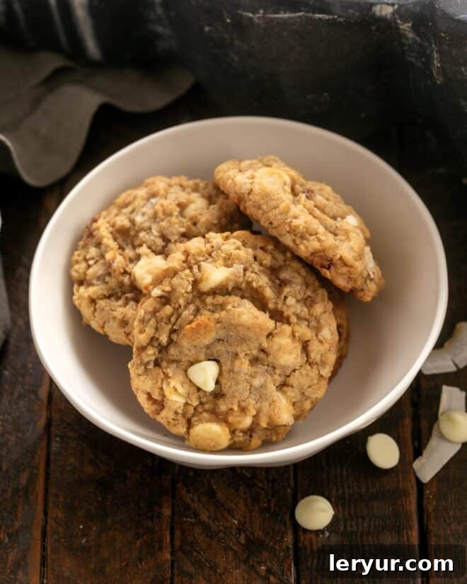 Chewy Oatmeal Toffee Cookies with a coconut bonus - fabulous flavors and textures in every bite make for truly irresistible cookies! Three enticing Oatmeal Toffee Cookies nestled in a small, rustic white ceramic bowl, showcasing their golden color and tempting texture, ready to be enjoyed.