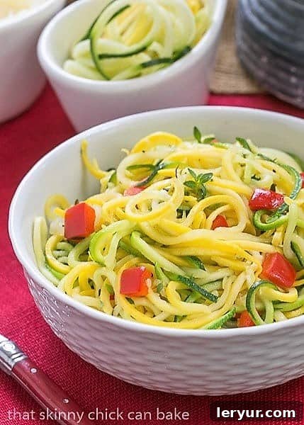 Zucchini Noodles with Parmesan - A light, healthy side dish! Only takes minutes to make! Close-up of Zucchini Noodles with Parmesan in a white basket weave bowl, ready to be enjoyed with a red handle fork.