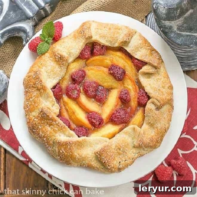 Overhead view of a beautifully baked Peach Raspberry Galette on a white ceramic cake stand, showcasing its golden crust and vibrant fruit filling, perfect for a summer dessert.