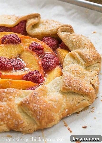 A delectable Peach Raspberry Galette, freshly baked and resting on a parchment-lined baking sheet, with sweet fruit juices bubbling around the edges of the flaky pastry.