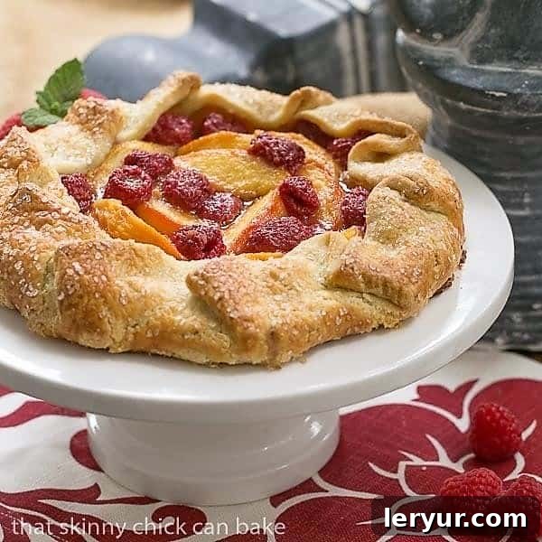 A tempting slice of Peach Raspberry Galette on a white plate, served warm with a scoop of creamy vanilla ice cream, ready to be enjoyed as a delightful dessert.