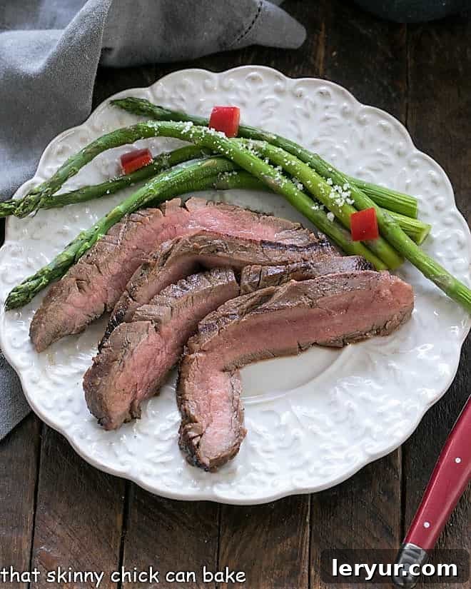 Easy Grilled Flank Steak slices on a white dinner plate with aspargus
