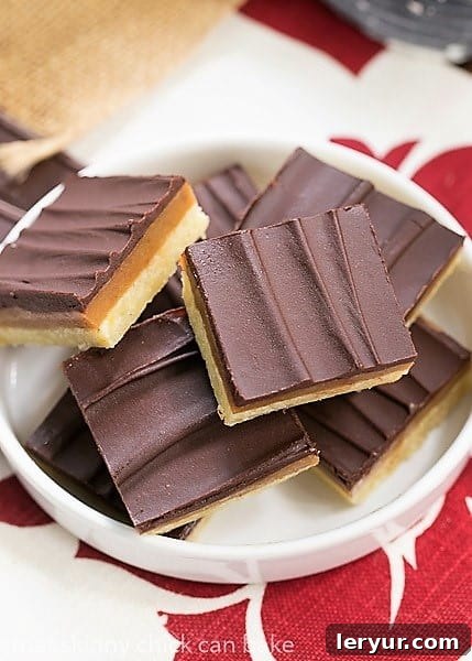 Two Ganache Topped Caramel Bars on a rimmed white plate, ready to be enjoyed.