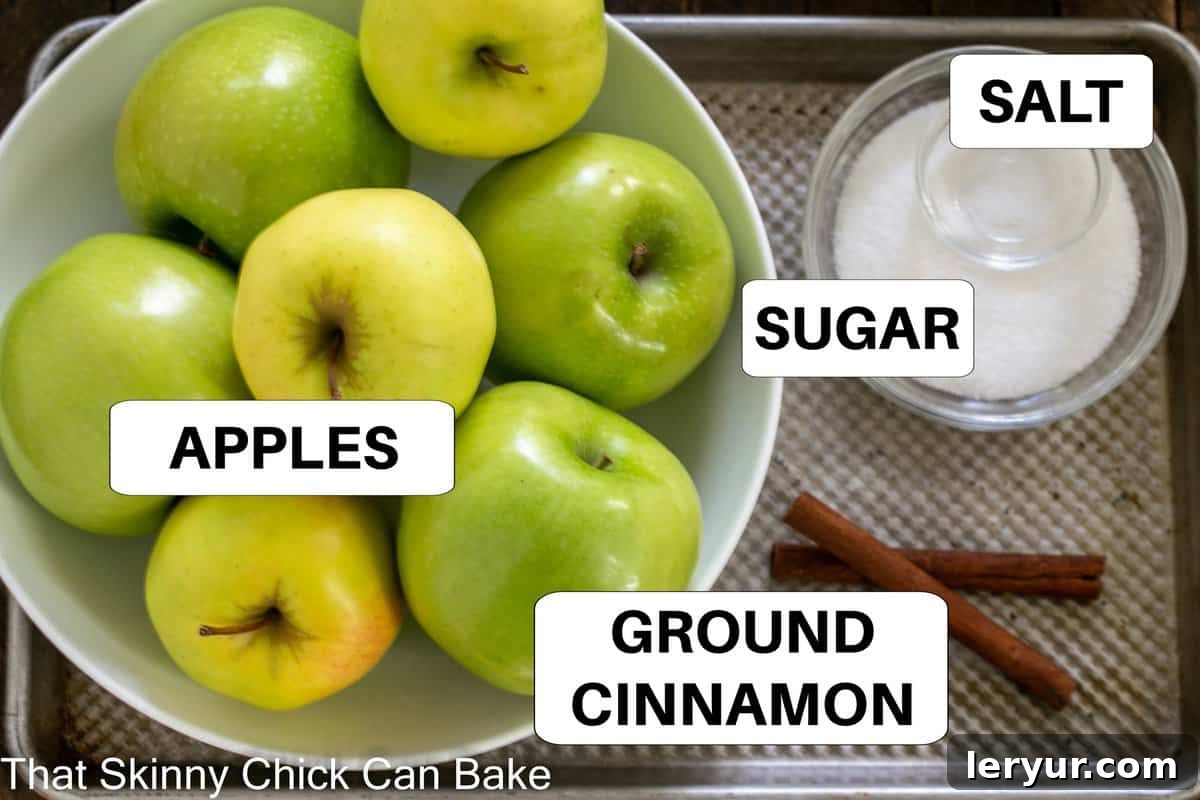 A simple array of applesauce ingredients laid out on a sheetpan, including apples, sugar, and cinnamon sticks.