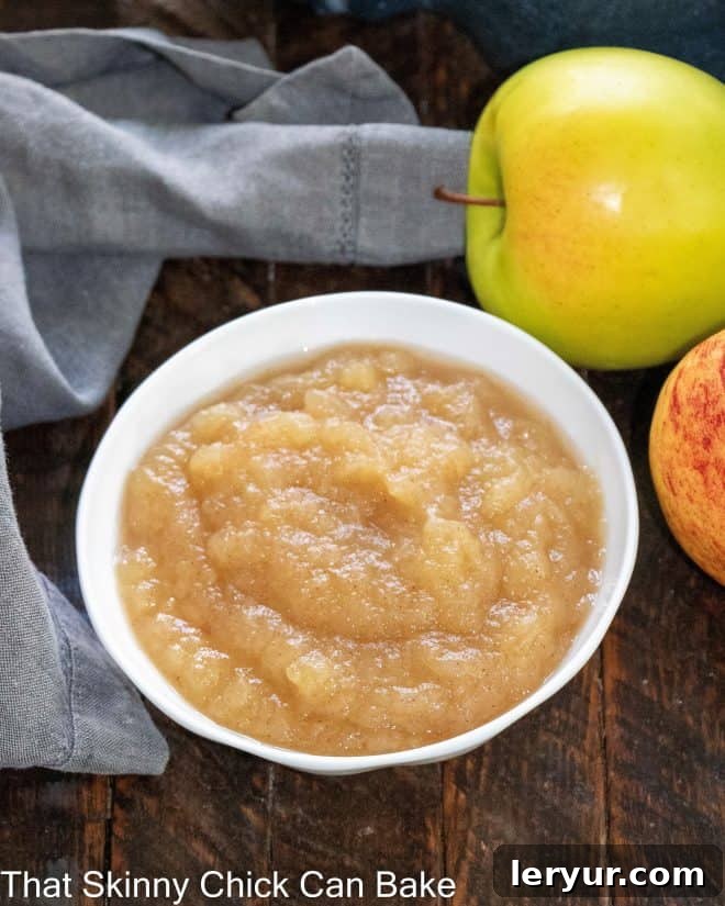 Overhead view of a small bowl of apple sauce next to two fresh apples, emphasizing the natural ingredients.