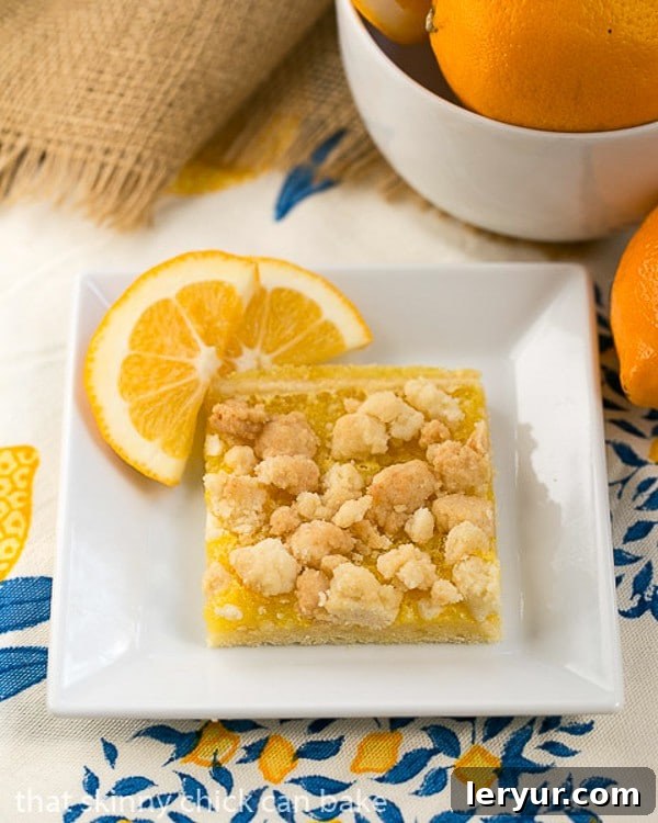 Scrumptious Meyer lemon bars featuring a golden sugar cookie crumble topping, zesty lemon filling, and a buttery shortbread crust. Meyer Lemon Streusel Bars on a white dish garnished with lemon slices, showcasing their distinct layers.
