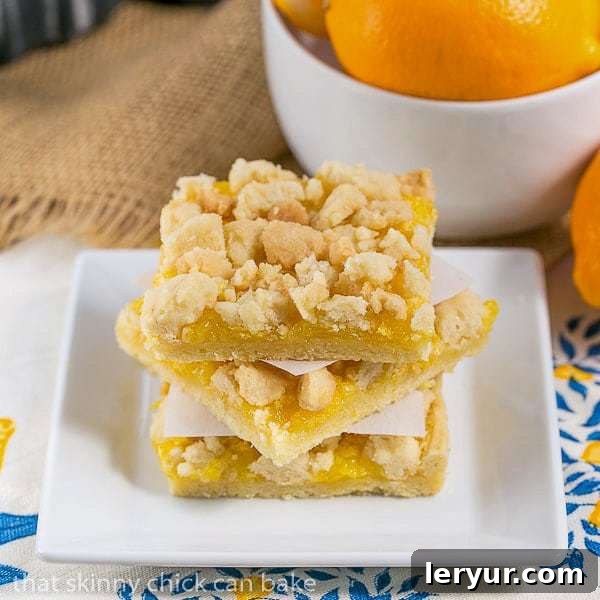 Meyer Lemon Streusel Bars - A scrumptious lemon bar with a sugar cookie crumble topping A stack of Meyer Lemon Streusel Bars on a square white plate, with a perfectly golden crumb topping.