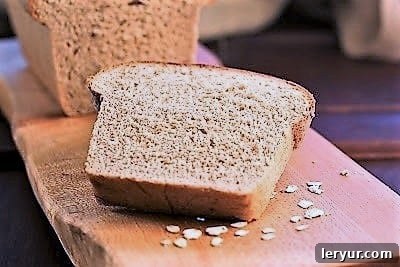 A beautiful slice of honey oat bread on a cutting board, showcasing its perfectly baked crust and soft interior.