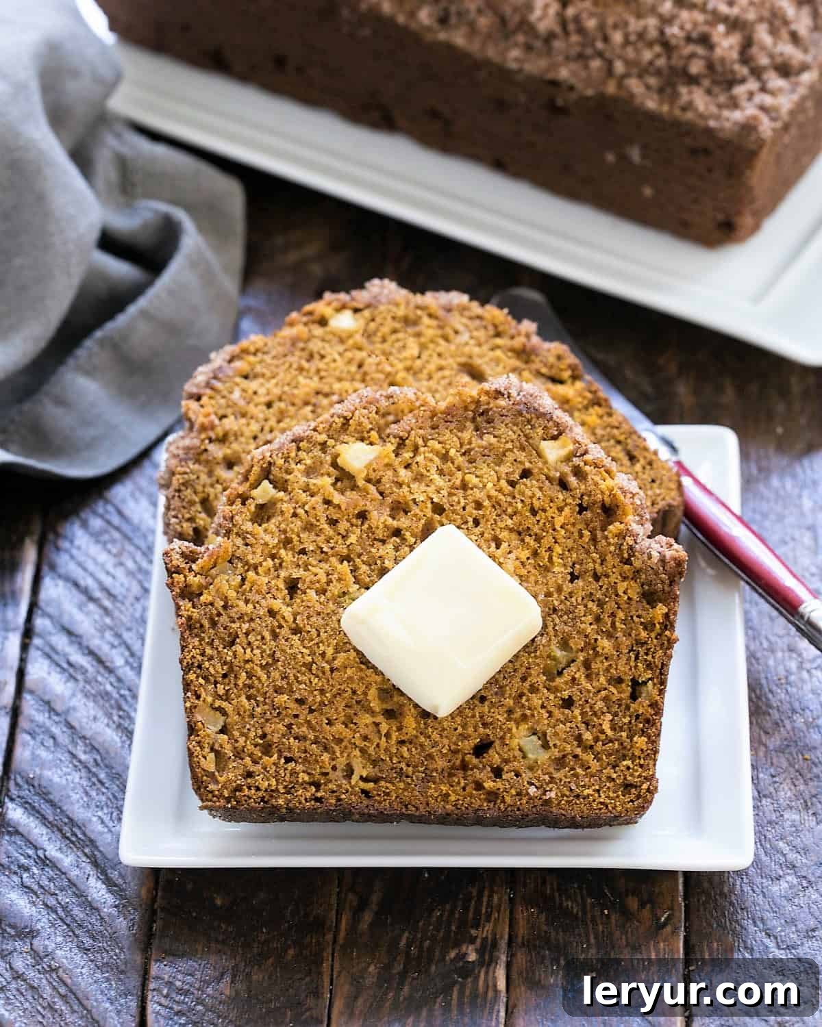 2 slices of an easy pumpkin bread on a white plate in front of a loaf of pumpkin bread on a tray.