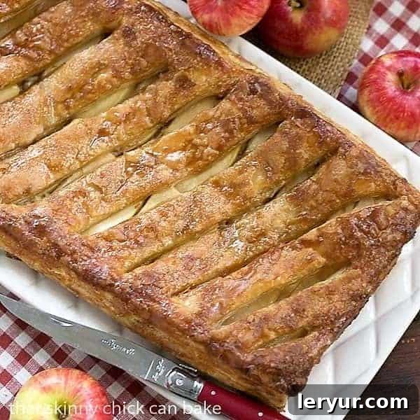 An inviting overhead shot of the entire Maple Glazed Apple Tart, beautifully golden brown with a shimmering glaze, resting on a rustic red and white checkered napkin, highlighting its rustic elegance.
