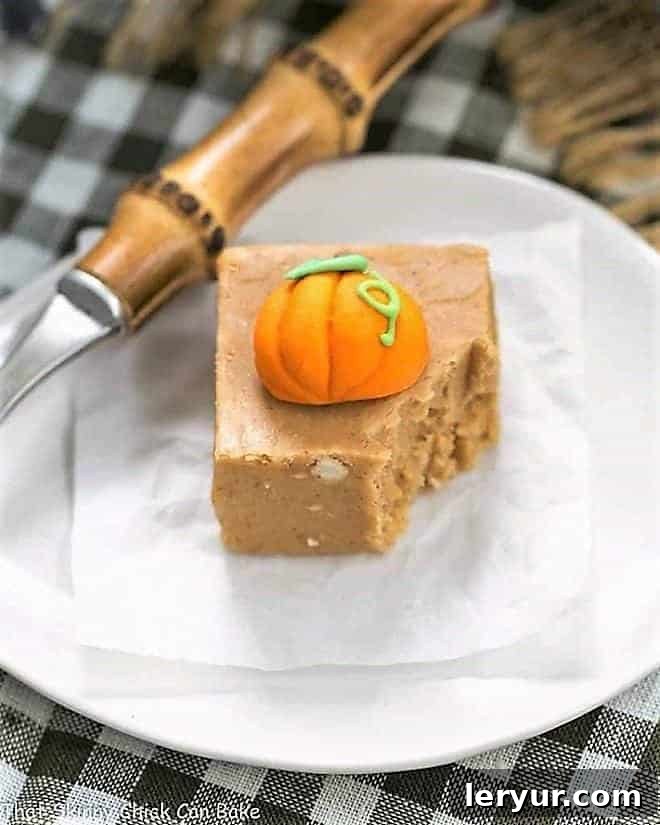 Pumpkin Fudge Recipe - A simple, autumn spiced candy! Easy Pumpkin Fudge on a white plate, topped with a candy pumpkin with a forkful removed.