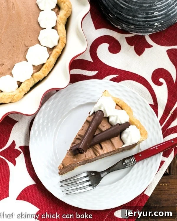 Overhead view of a slice of French Silk Pie on a white plate with a red handled fork. Garnished with chocolate shavings and a dollop of whipped cream.