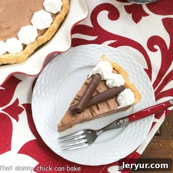 A slice of Classic French Silk Pie on a plate on a red and white napkin. Garnished with whipped cream and chocolate curls.