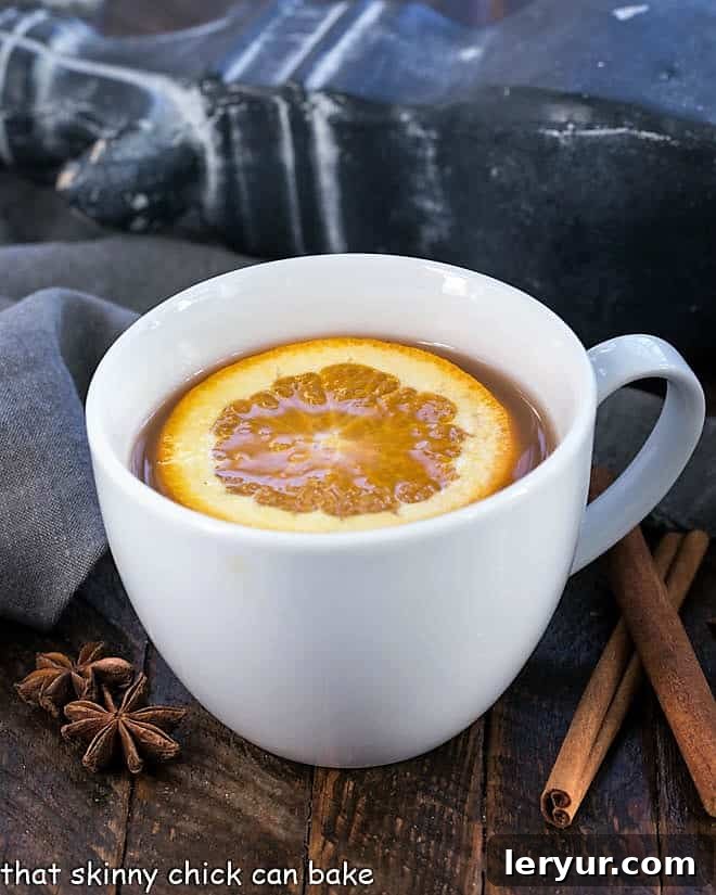 Mulled Apple Cider in a round mug, topped with a fresh orange slice and a cinnamon stick.