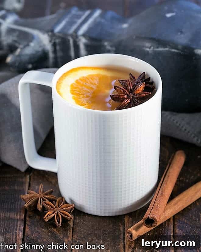 Hot apple cider in a white mug garnished with a slice of orange and a cinnamon stick