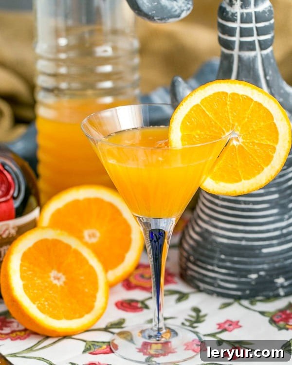Elevated Grand Marnier Mimosas 7 Grand Marnier Mimosas in a glass pitcher with a glass garnished with an orange slice and orange halves in the foreground