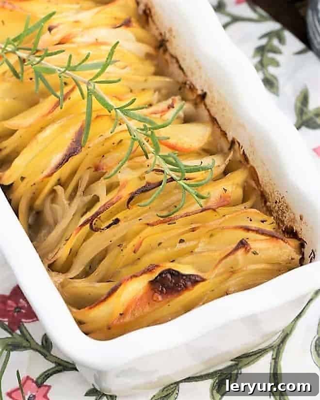 Close view of a hasseback potato casserole with a sprig of rosemary in a white baking dish, ready to serve.